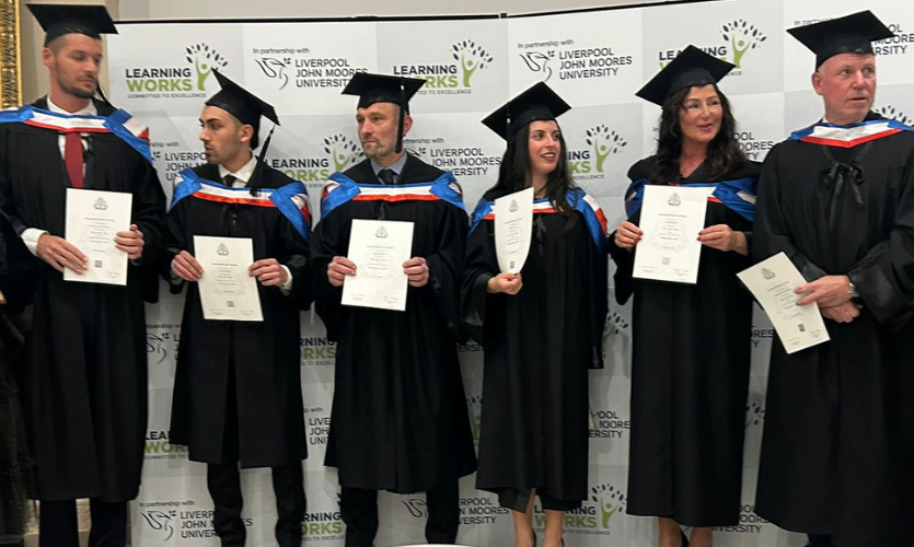 Six graduates wearing black gowns and caps all holding certificates in front of their bodies 