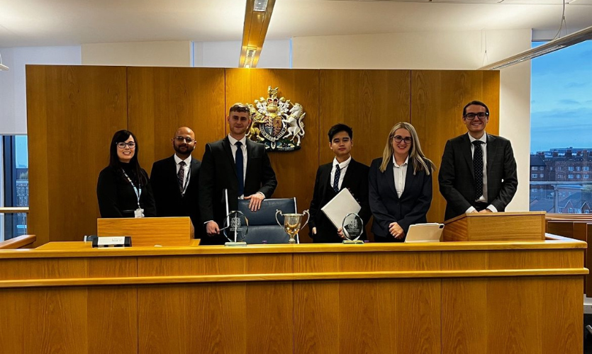 Six people stood in a row on a wooden platform, or the Judge's bench in LJMU's mock courtroom